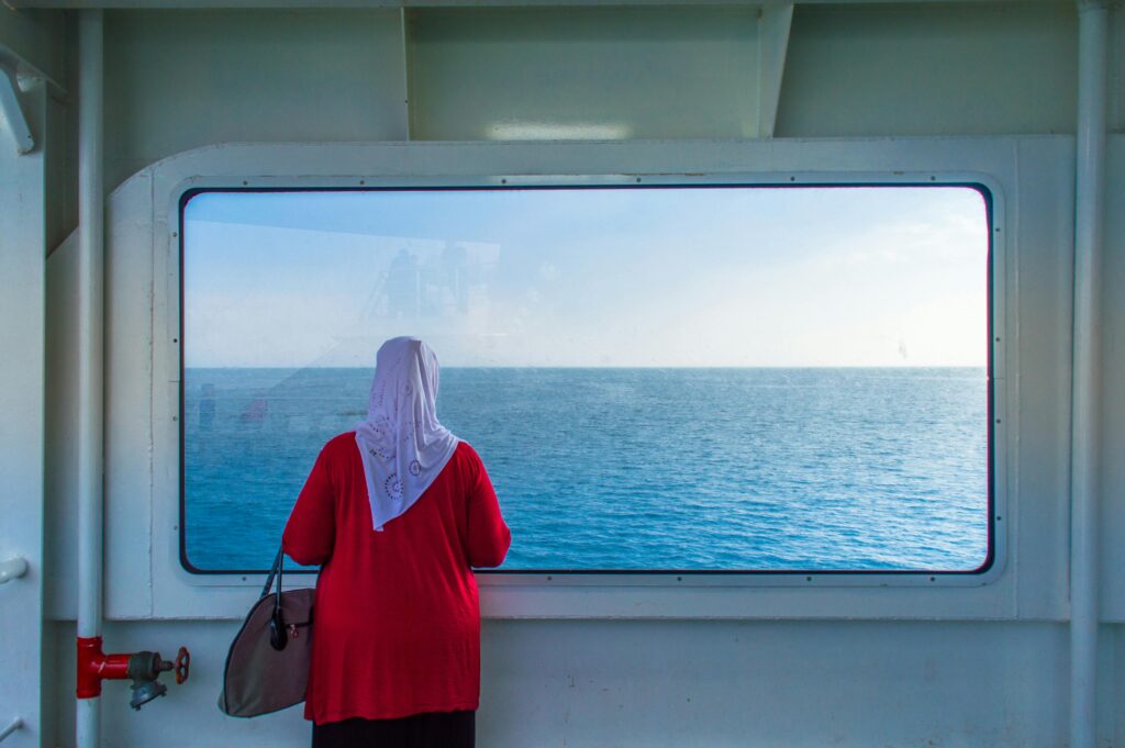 A woman gazing out the window of a cruise ship at the serene sea horizon.