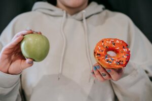 A person holding both an apple and a donut, symbolizing a food choice dilemma.