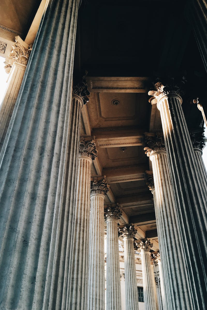 Dramatic upward shot of classic stone columns lit by sunlight with ornate details.