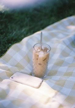 Chilled iced coffee with a straw on a plaid blanket, perfect for a sunny summer picnic.