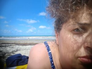 A close-up, natural light self-portrait of me relaxing at the beach, with the ocean waves and a clear blue sky in the background, capturing a moment of restorative immersion.